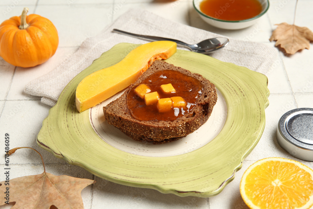 Plate of toast with sweet pumpkin jam and orange on white tile background