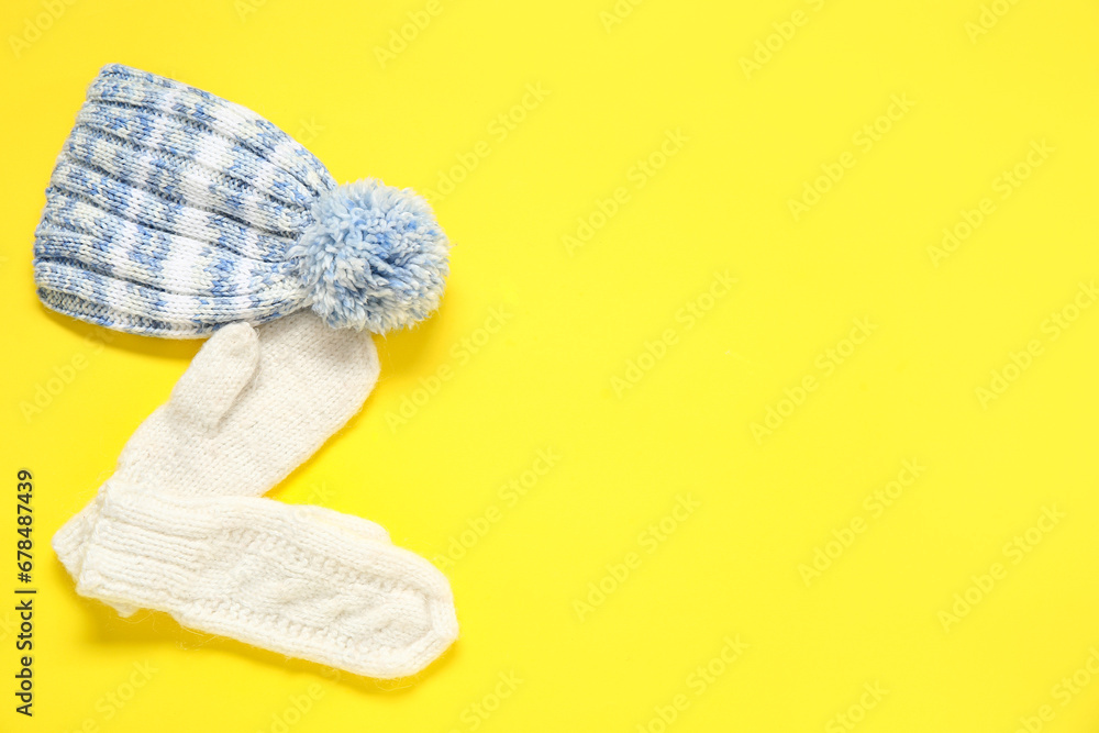 Stylish knitted hat and mittens on yellow background