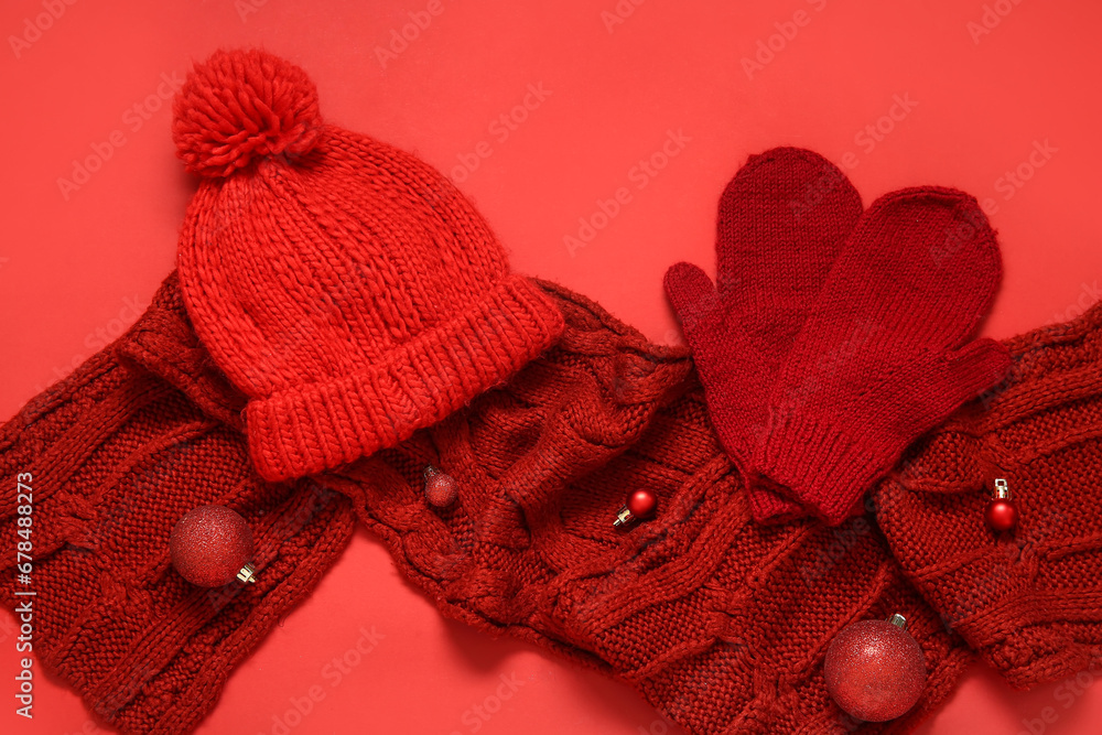 Composition with warm mittens, hat, scarf and Christmas balls on red background