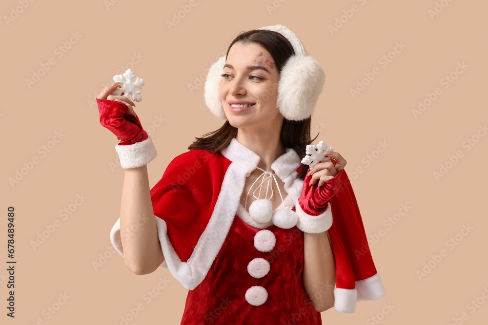 Beautiful young woman dressed as Santa Claus with decorative snowflakes on beige background