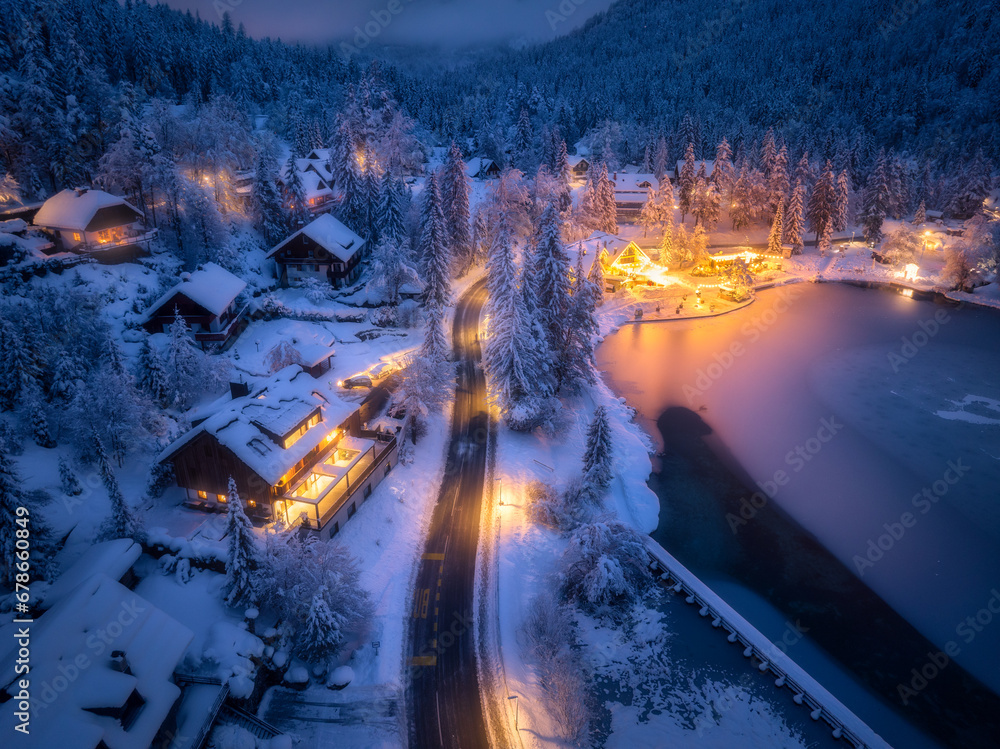 Aerial view of fairy town in snow, road, forest, Jasna lake and houses with lights at night in winte