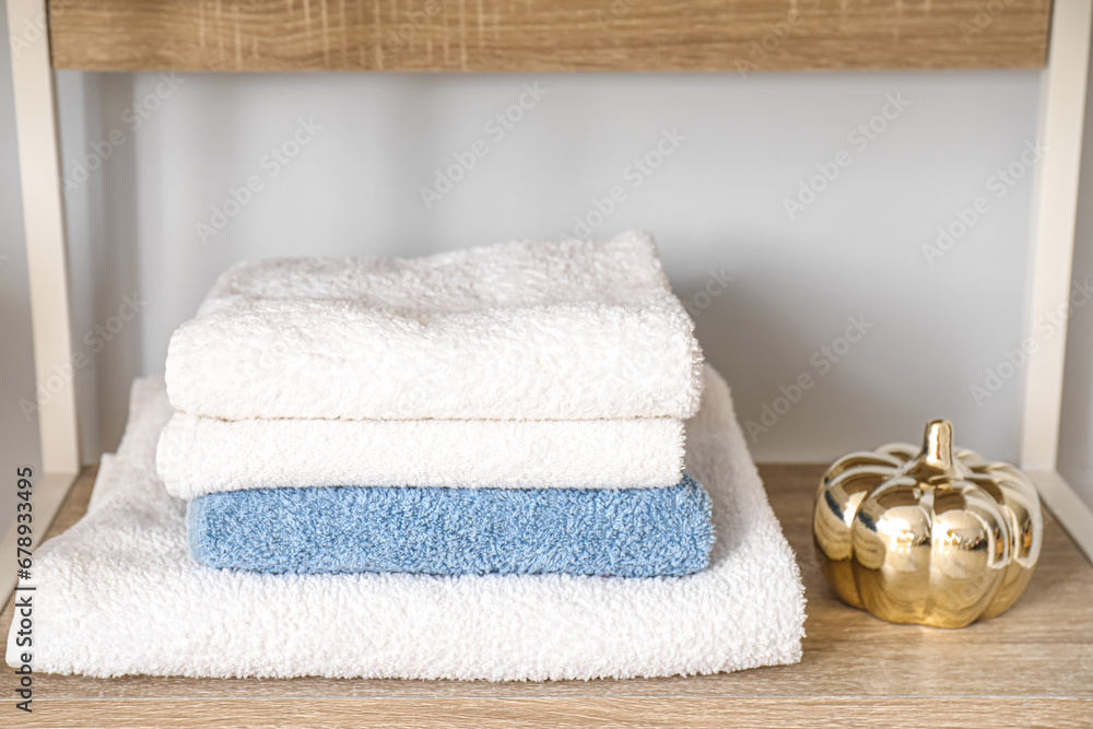 Stack of clean towels and decor on shelf against light wall, closeup