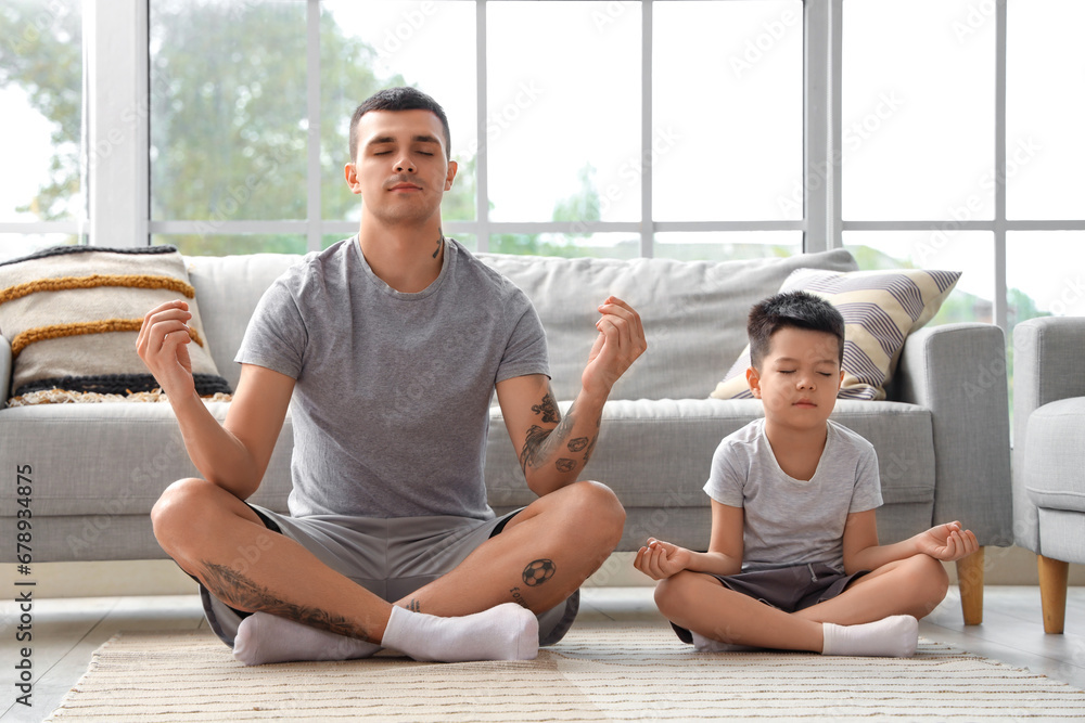 Young man with his little son meditating at home