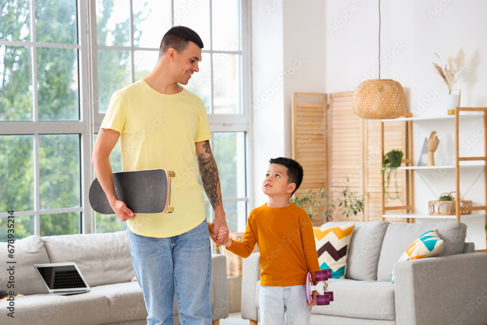 Young man and his little son with skateboards at home