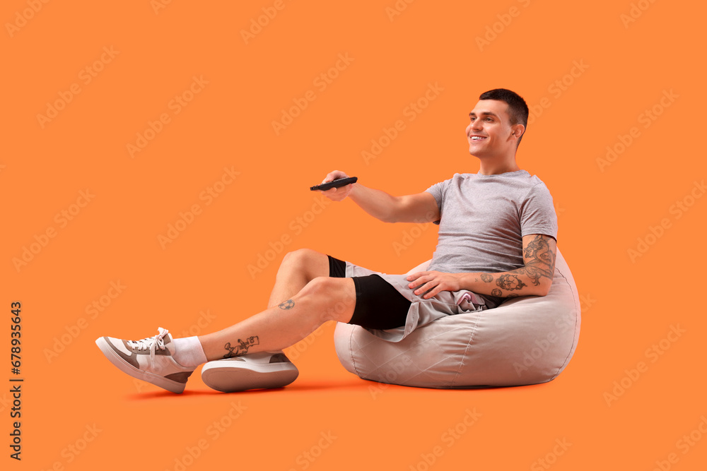 Young man watching TV on orange background