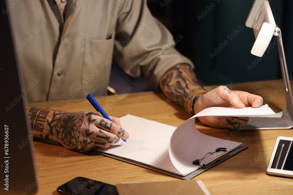 Young tattooed man working in office at night, closeup