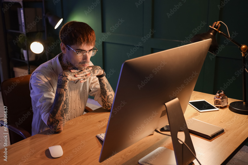 Young tattooed man working in office at night