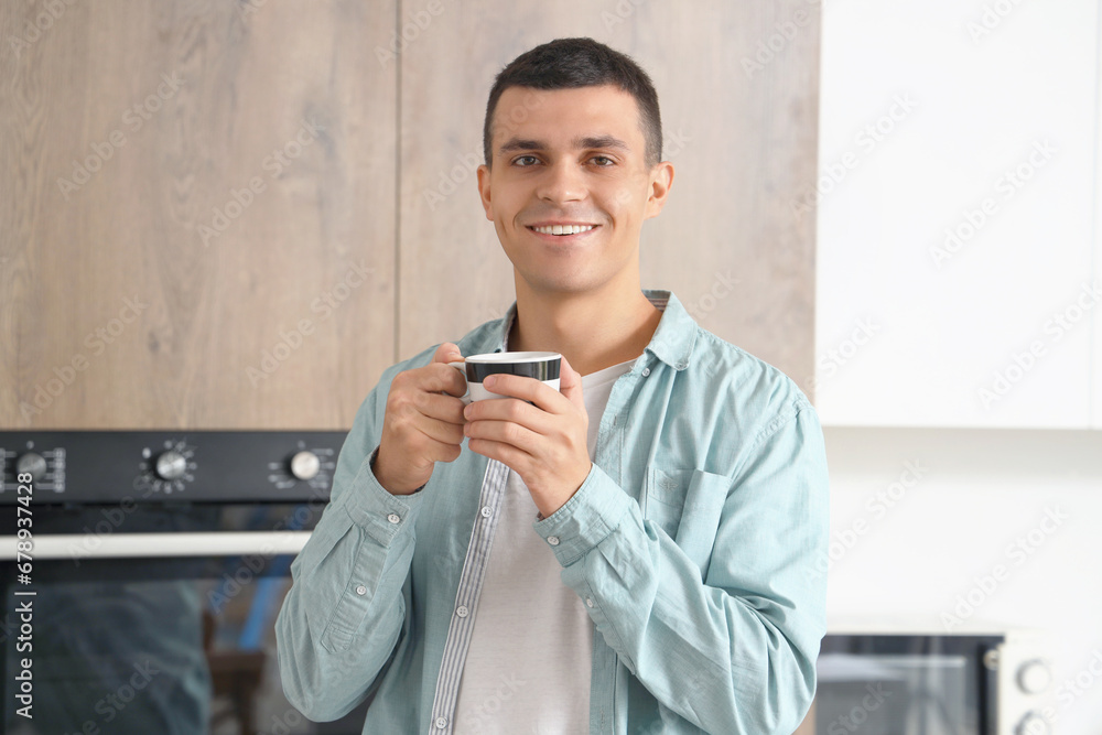 Handsome young man with cup of coffee in kitchen at home