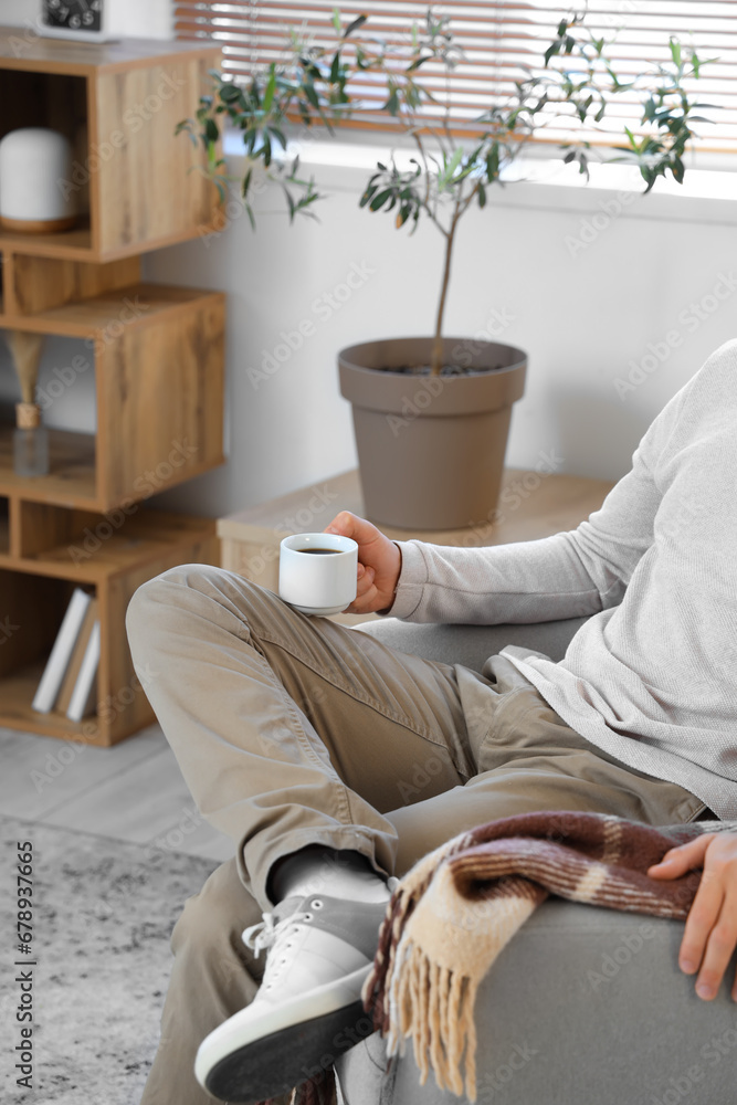 Young man with cup of coffee sitting on armchair in modern living room