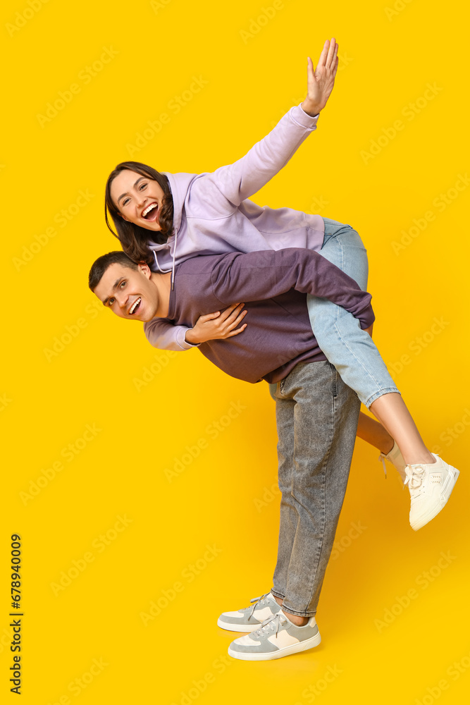 Happy young man giving piggyback ride to his girlfriend on yellow background