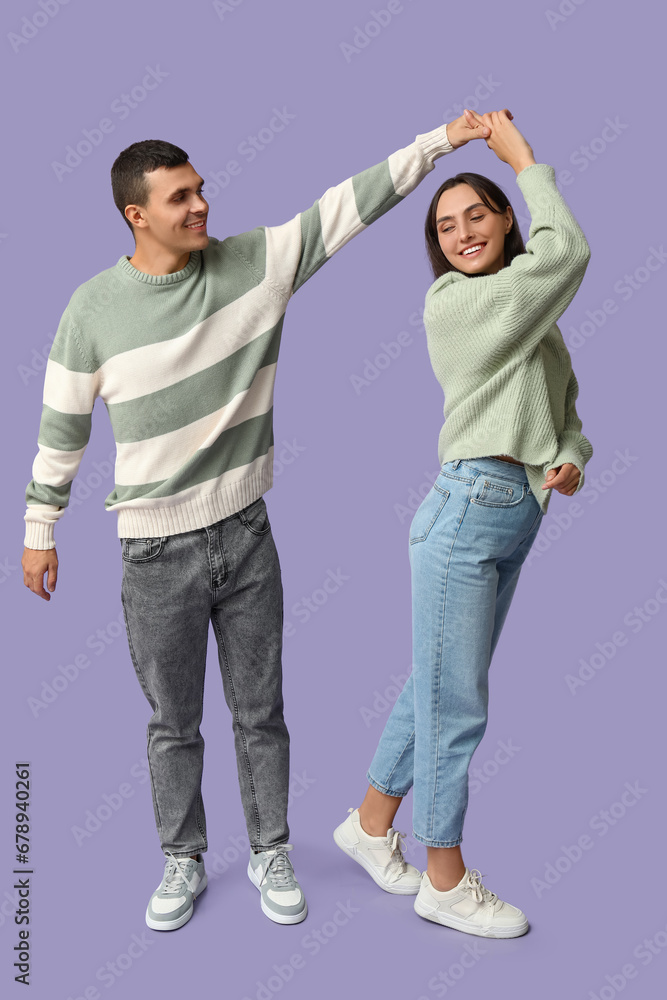 Happy young couple dancing together on lilac background