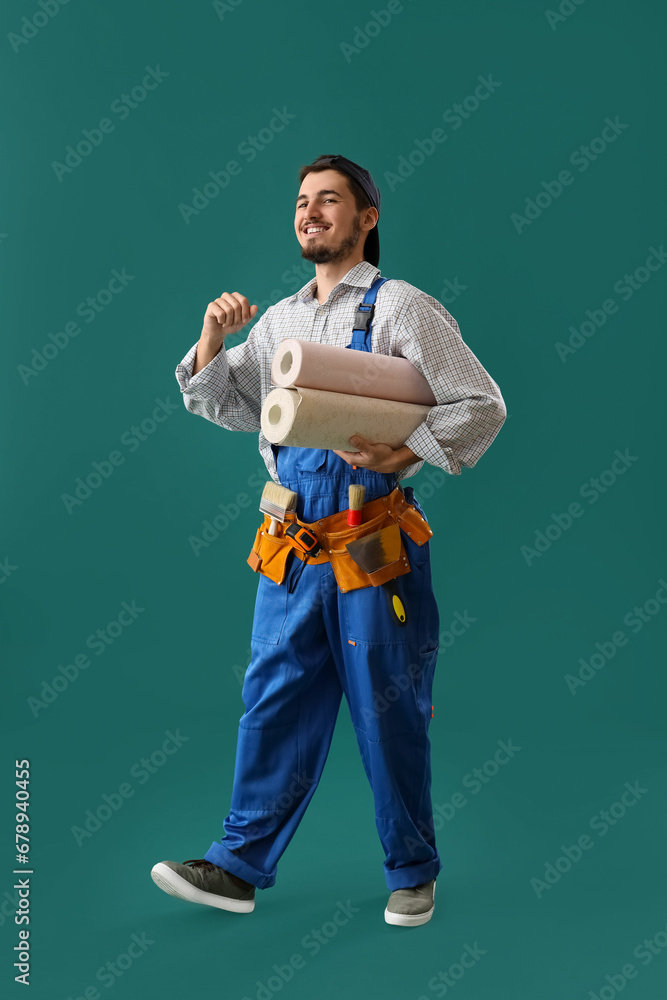 Male decorator with wallpaper rolls on green background