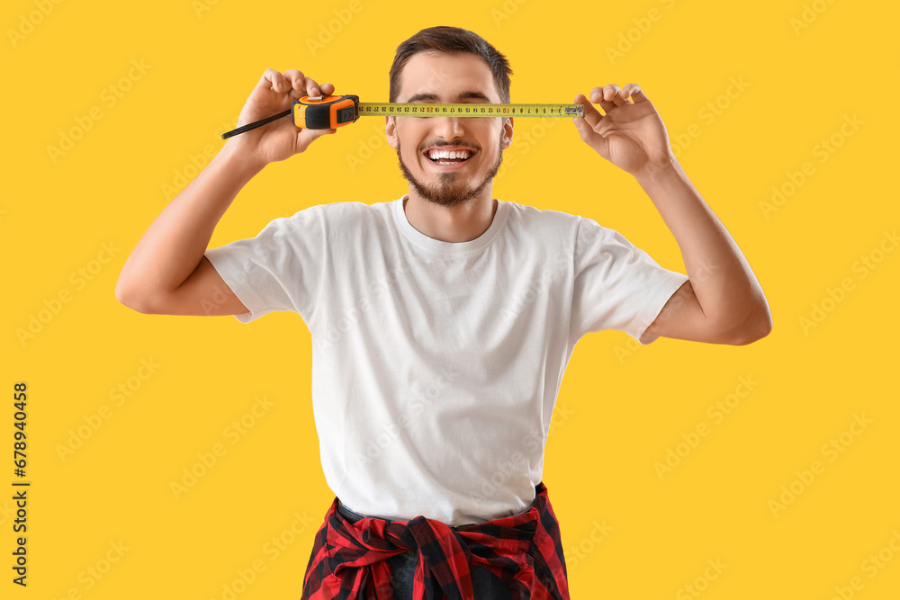 Young man with tape measure on yellow background