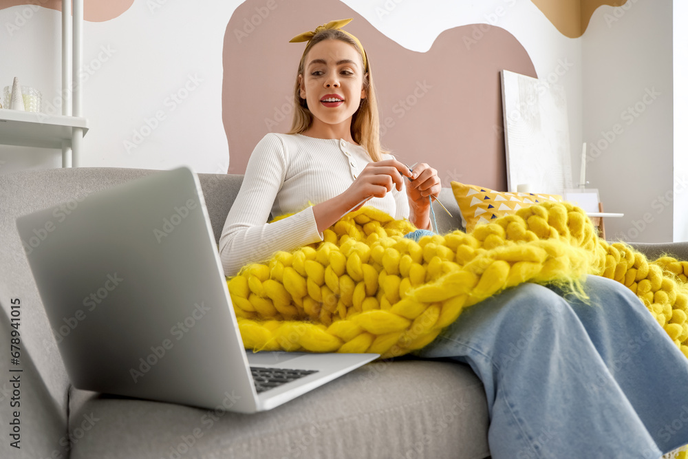 Young woman knitting with needles and laptop at home