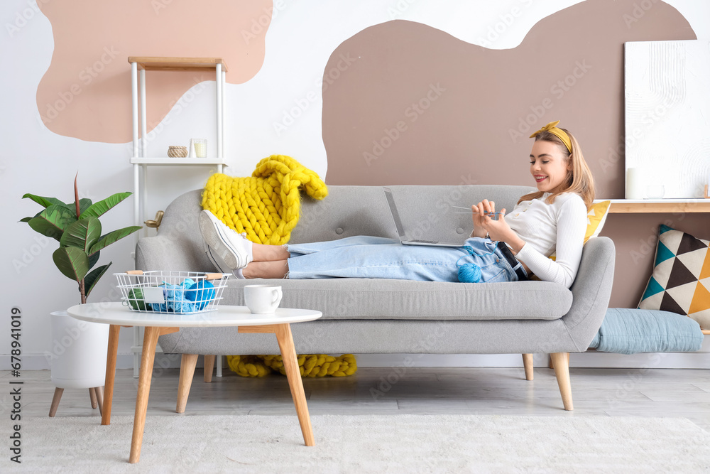 Young woman knitting with needles and laptop at home