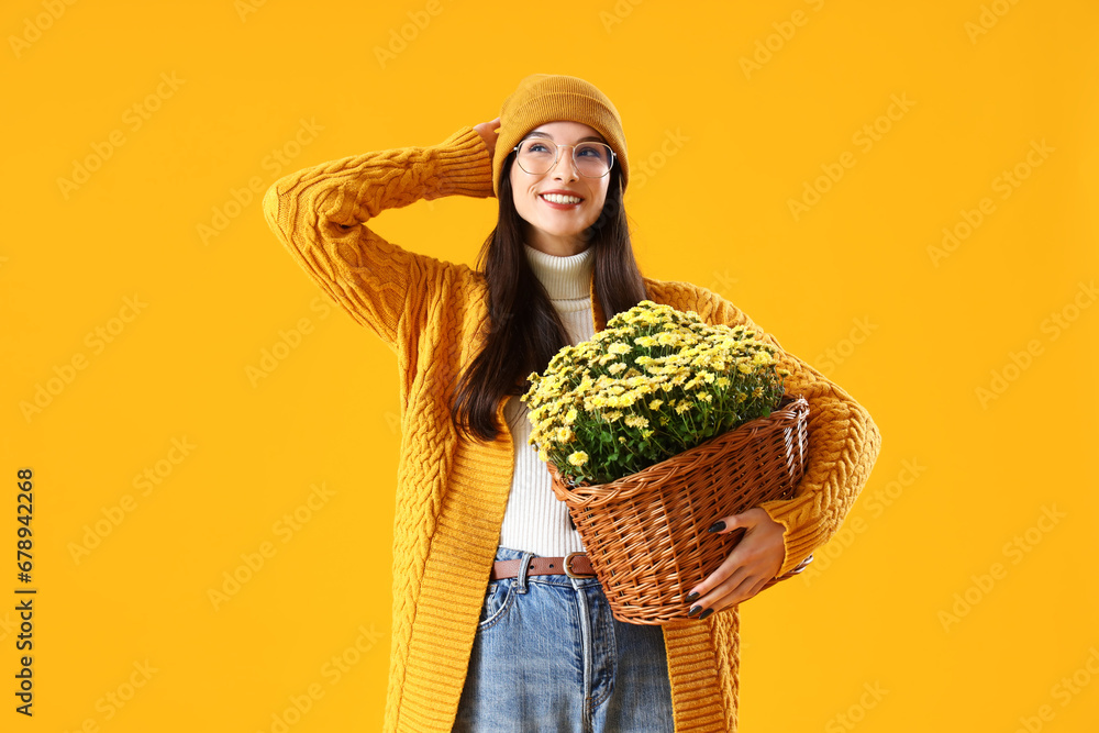 Stylish young woman with chrysanthemum flowers on yellow background