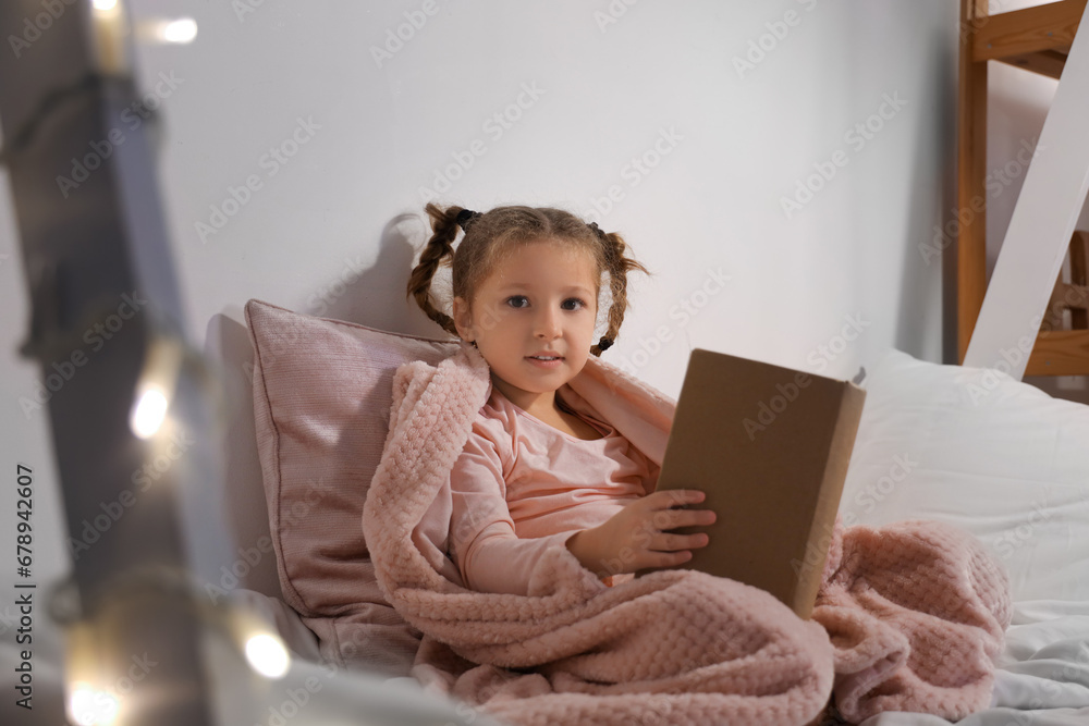 Cute little girl reading story in bedroom at night