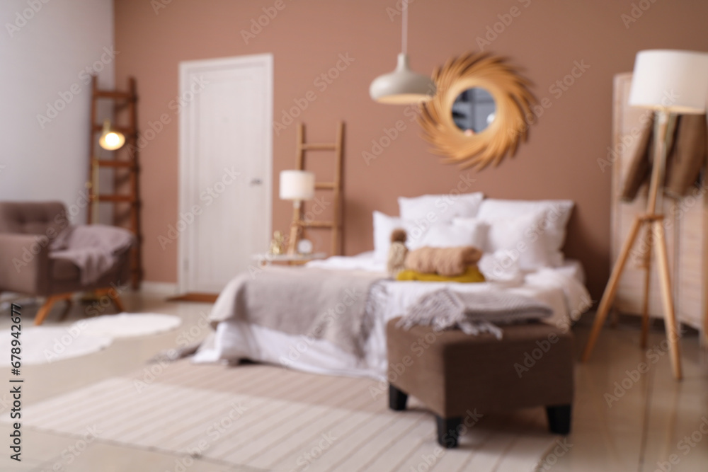 Blurred view of cozy bedroom with winter clothes on bed and lamps