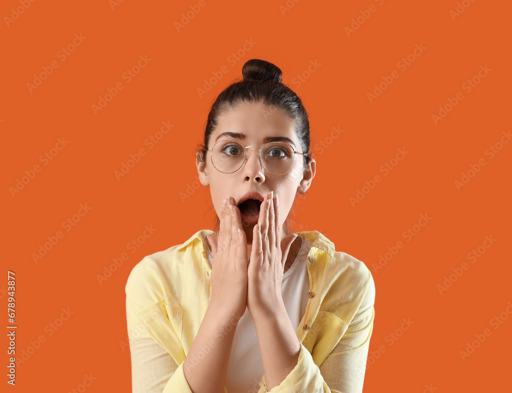 Shocked young gossip woman on orange background, closeup