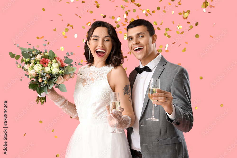 Young wedding couple with bouquet of flowers and champagne on pink background