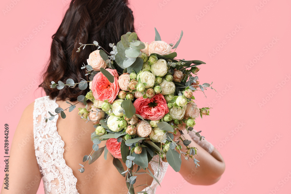 Beautiful bride with wedding bouquet on pink background, back view