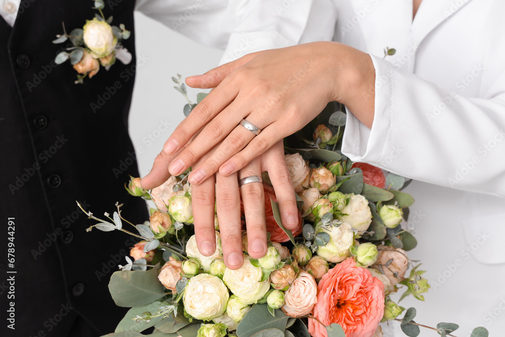 Married young couple with wedding rings and bouquet on light background, closeup