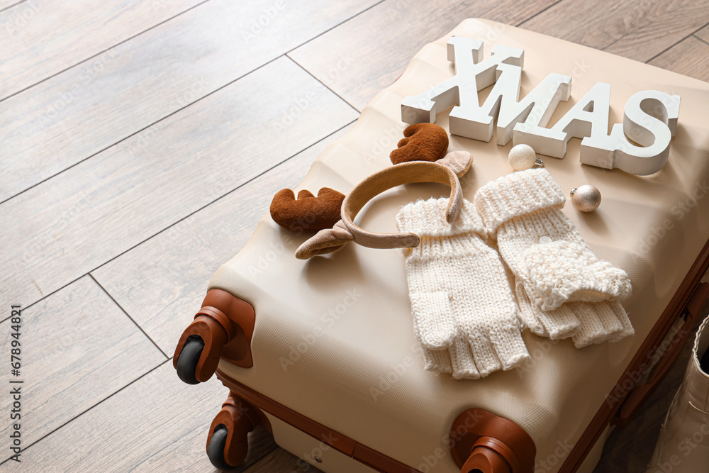 Stylish suitcase, word XMAS and decorations on wooden floor