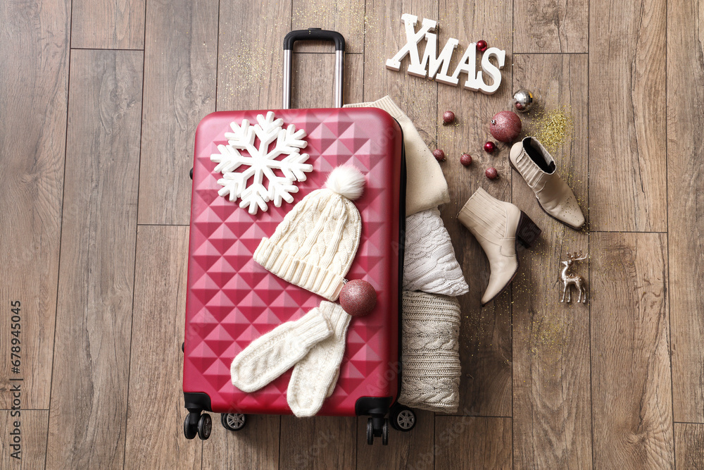 Composition with stylish suitcase, warm clothes and Christmas decorations on wooden floor