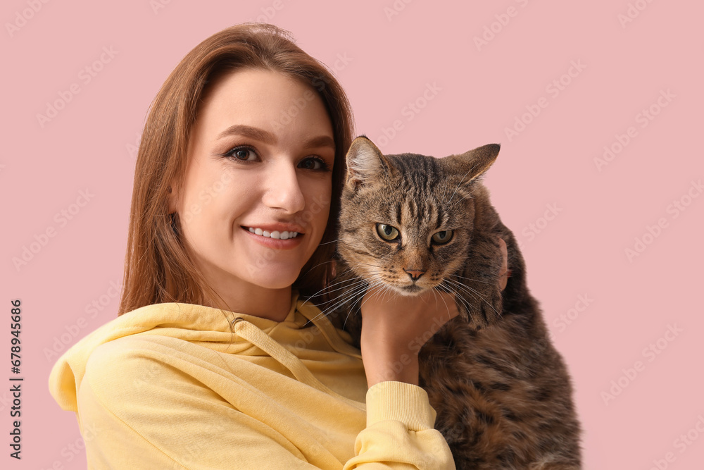 Pretty young woman with cute tabby cat on pink background, closeup