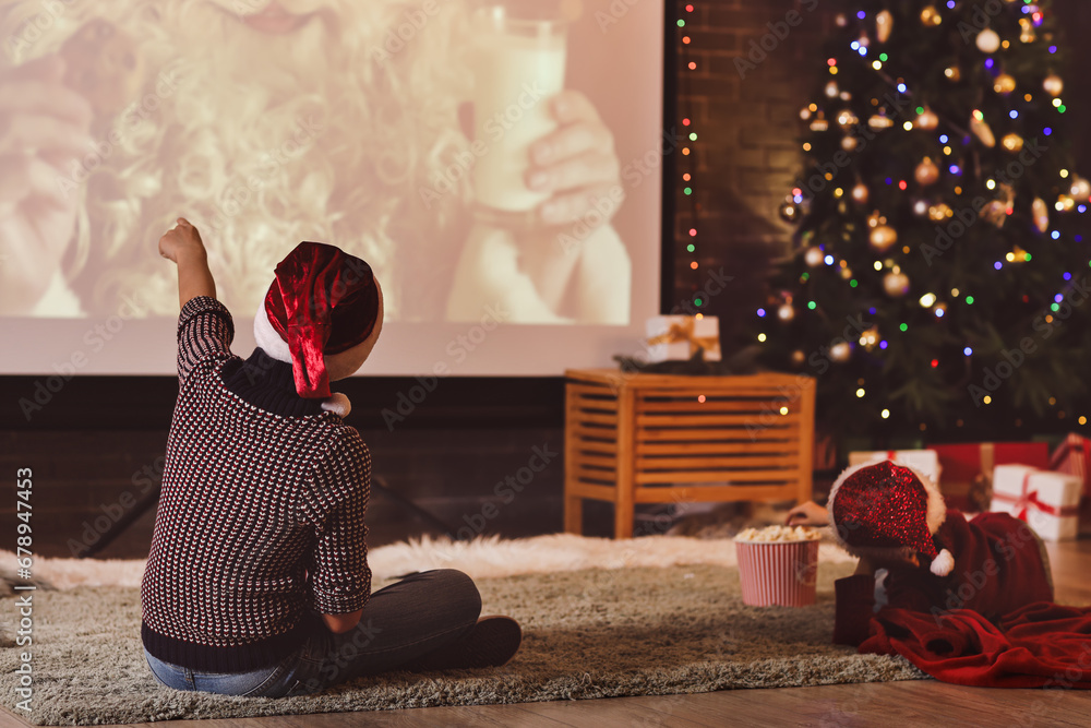 Little children with popcorn watching Christmas movie on projector screen at home, back view