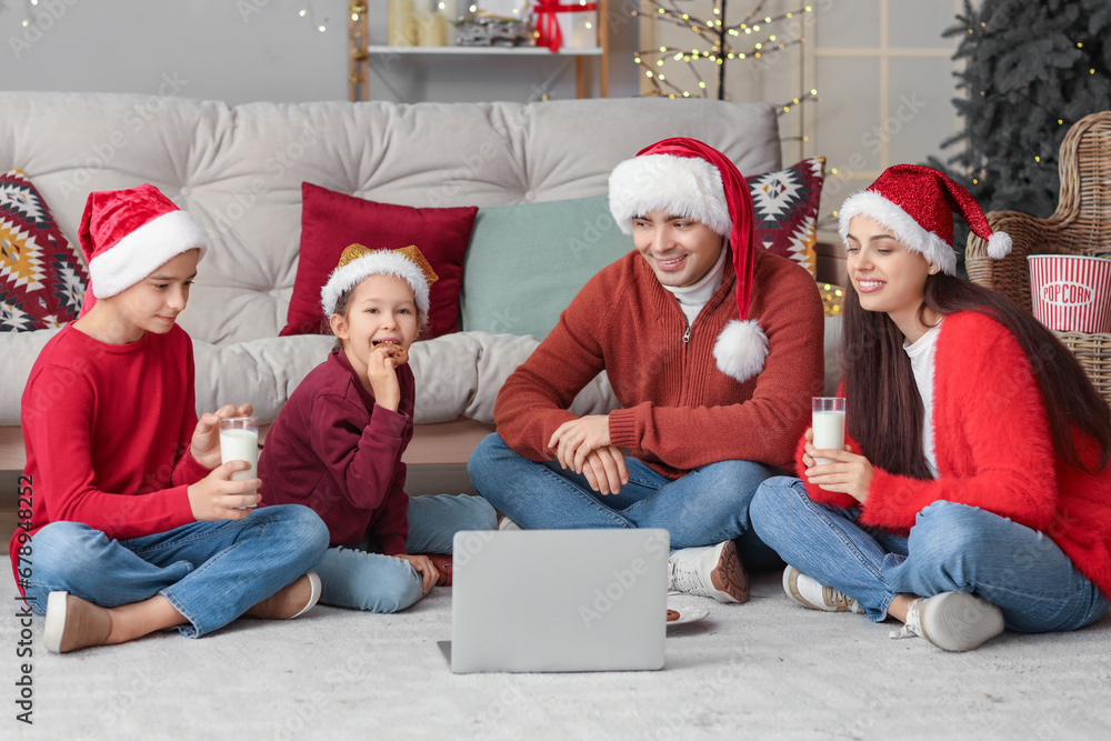 Happy family with milk and cookies watching Christmas movie on laptop at home