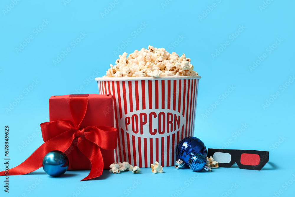 Bucket of popcorn with 3D glasses, gift box and Christmas balls on blue background