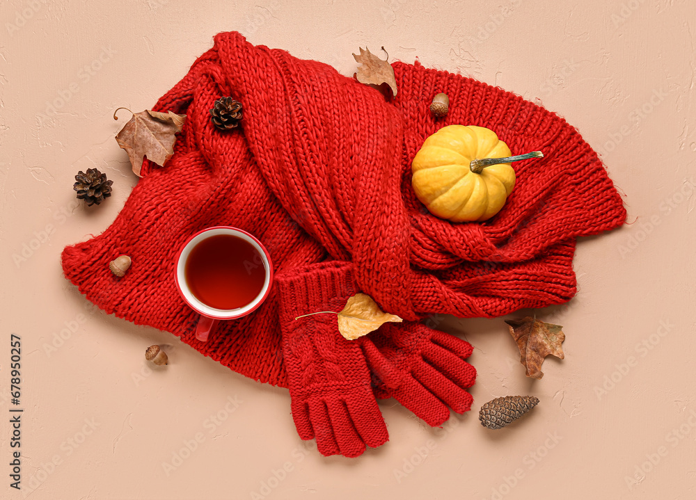 Cup of tea with gloves, scarf and autumn decor on beige background