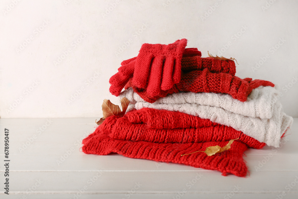 Gloves with scarves and leaves on wooden table against white background