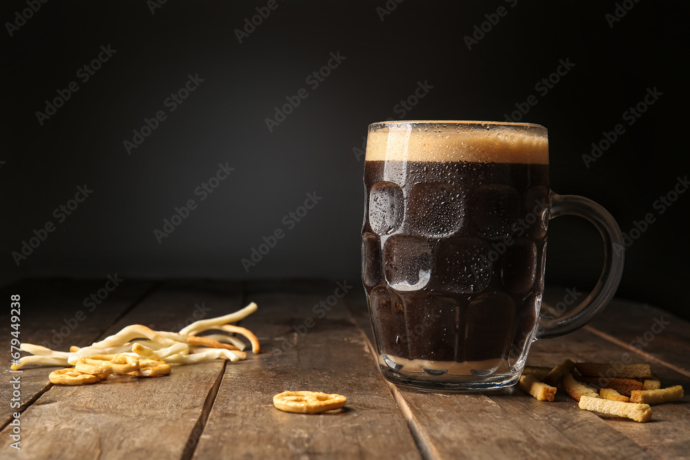 Mug of dark beer and snacks on table against black background