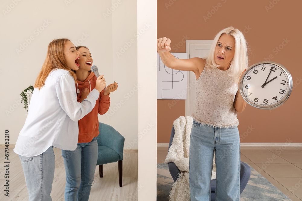 Mature woman with clock suffering from loud neighbours singing at home