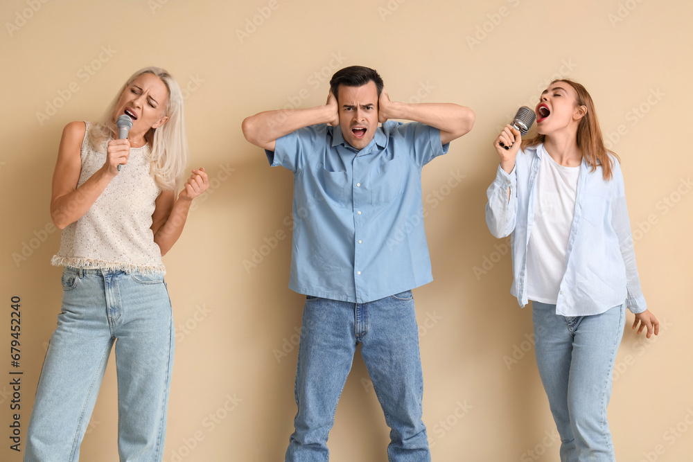 Young man suffering from loud neighbours singing on beige background