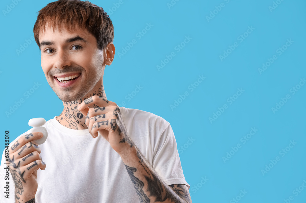 Young tattooed man with dental floss on blue background, closeup