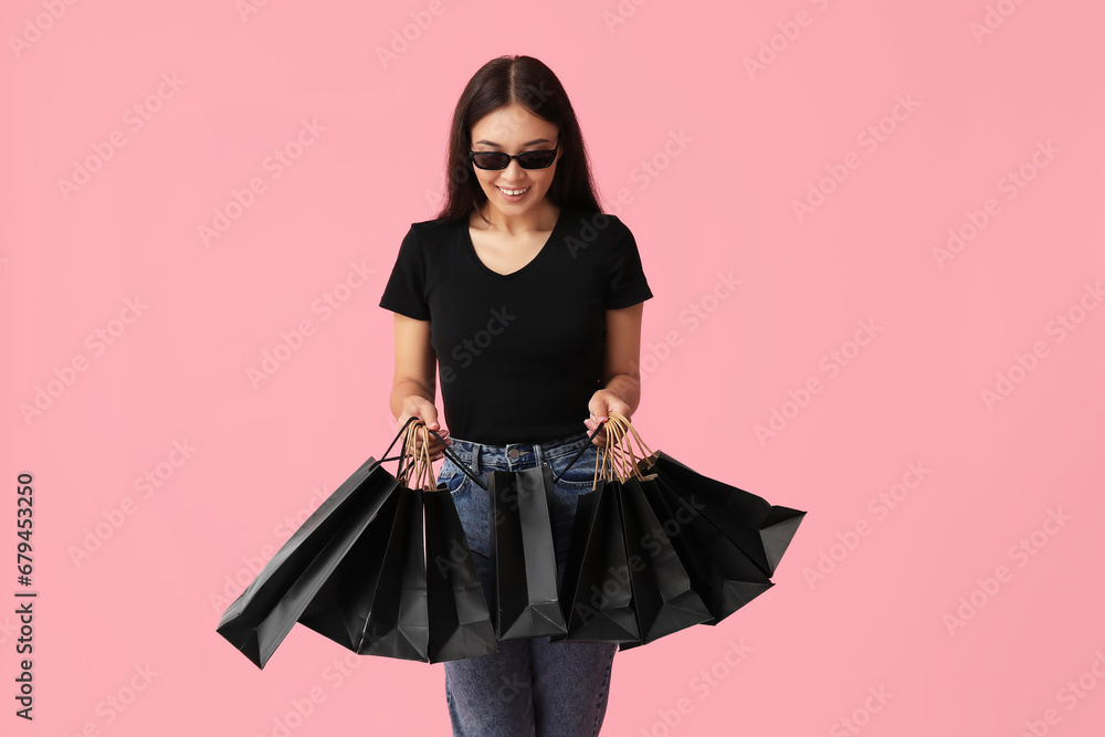 Beautiful young Asian woman with shopping bags on pink background. Black Friday sale