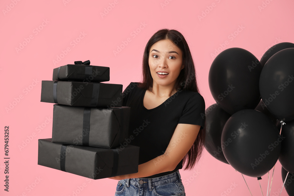 Beautiful young Asian woman with gift boxes and balloons on pink background. Black Friday sale