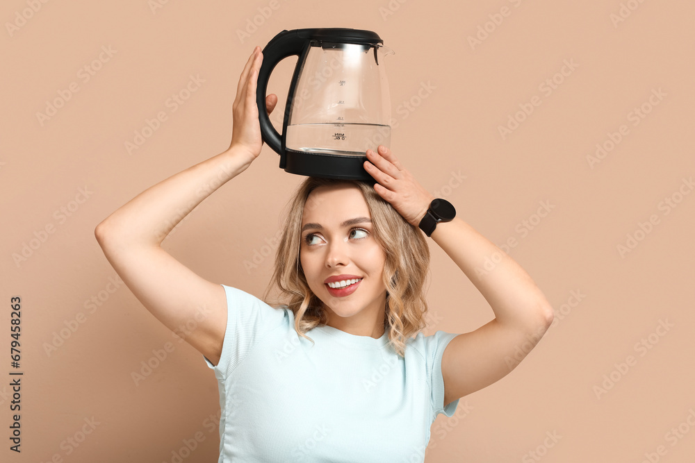 Funny young woman with modern electric kettle on beige background