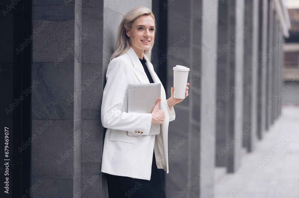 Successful businesswomen stand and drink coffee in a meeting outside an office building and work together happily.