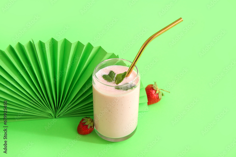 Glass of tasty strawberry smoothie with fan on green background