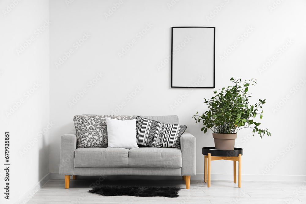 Interior of light living room with blank frame, grey sofa and houseplant