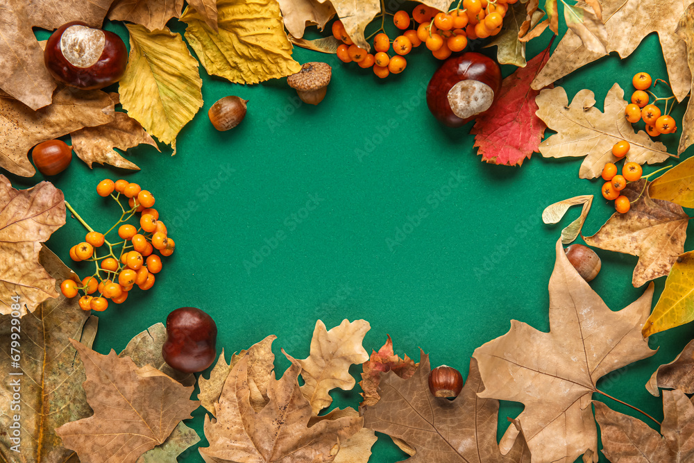 Frame made of autumn leaves with chestnuts, hazelnuts and rowan on green background