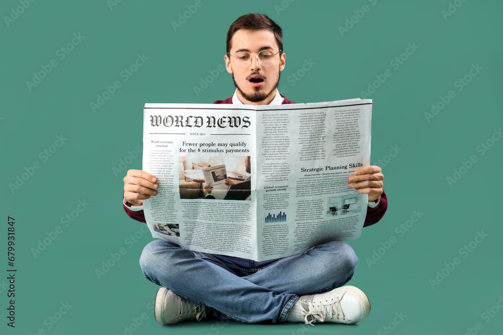 Shocked young man reading newspaper on green background