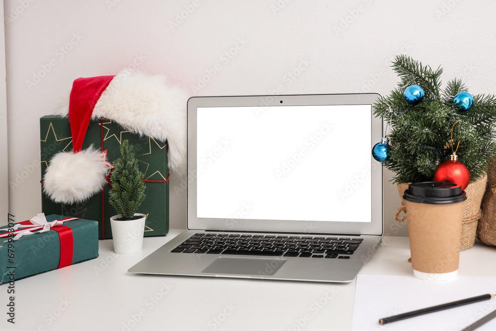 Workplace with blank laptop, presents and Christmas tree in office