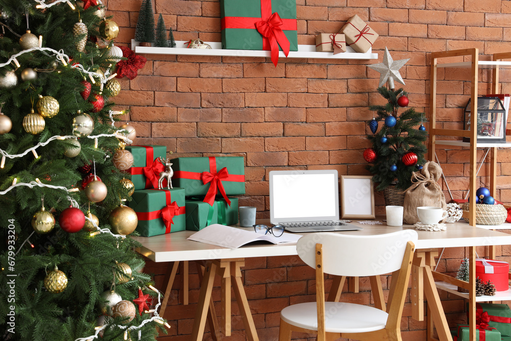 Modern workplace with blank laptop, presents and Christmas tree in office