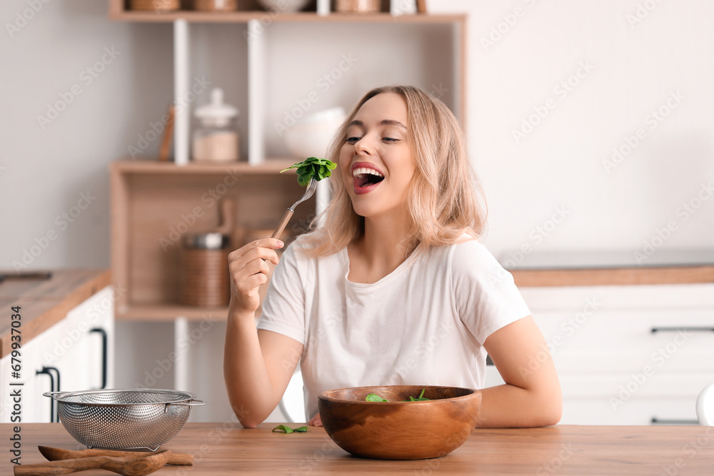 Beautiful sporty woman eating tasty vegetable salad in kitchen at home. Weight loss concept