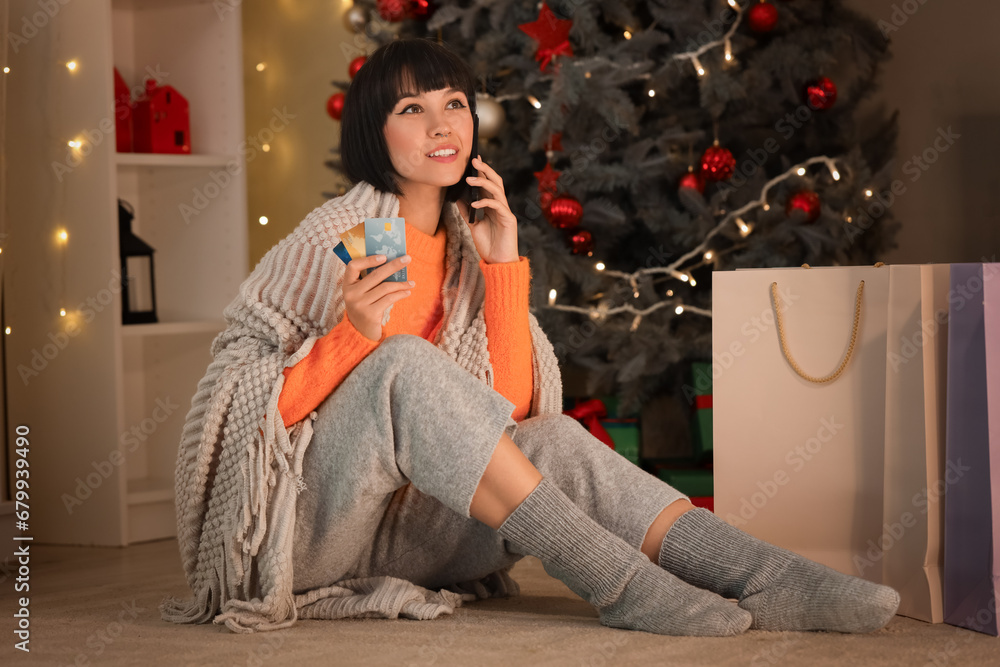 Young woman with mobile phone and credit cards shopping online for Christmas at home